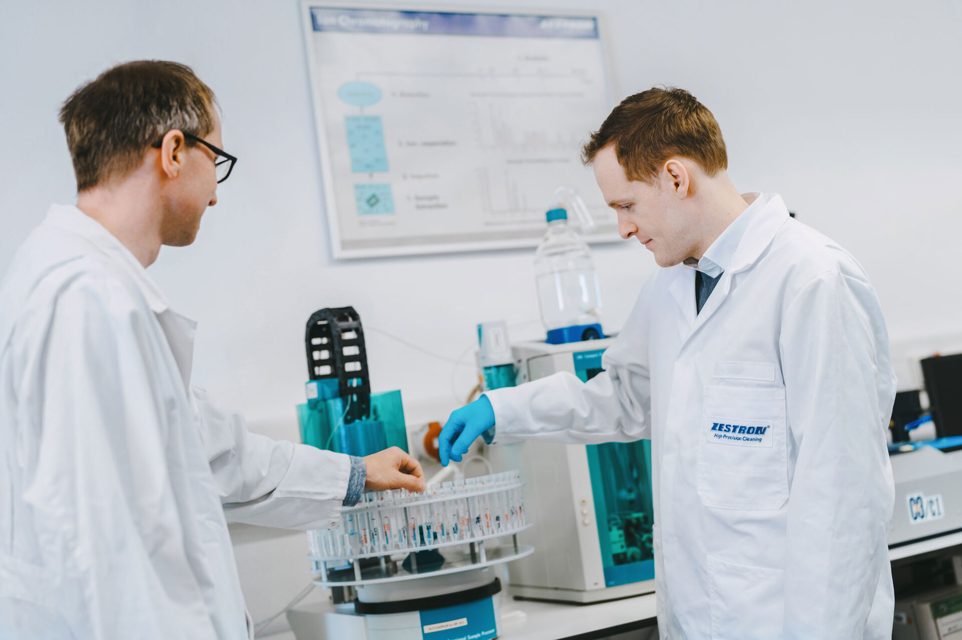 Zwei Ingenieure stehen vor dem Ionenchromatographie Analysegerät, um die ionische Kontamination auf einer Leiterplatte zu überprüfen. | © @The Sour Cherry Fotografie - Michaela Curtis