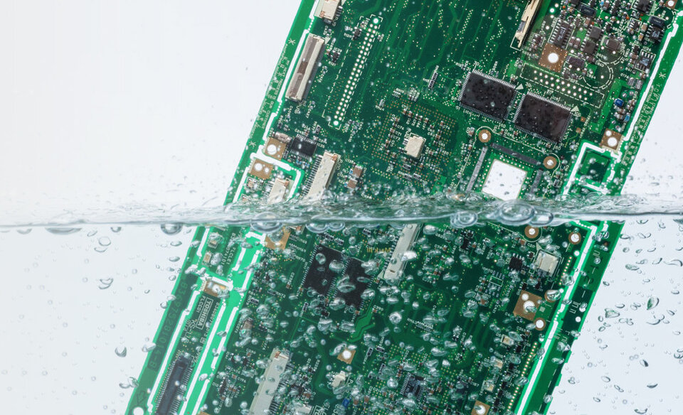 Eine grüne Leiterplatte ist umgeben von Wasser und Luftblasen. 