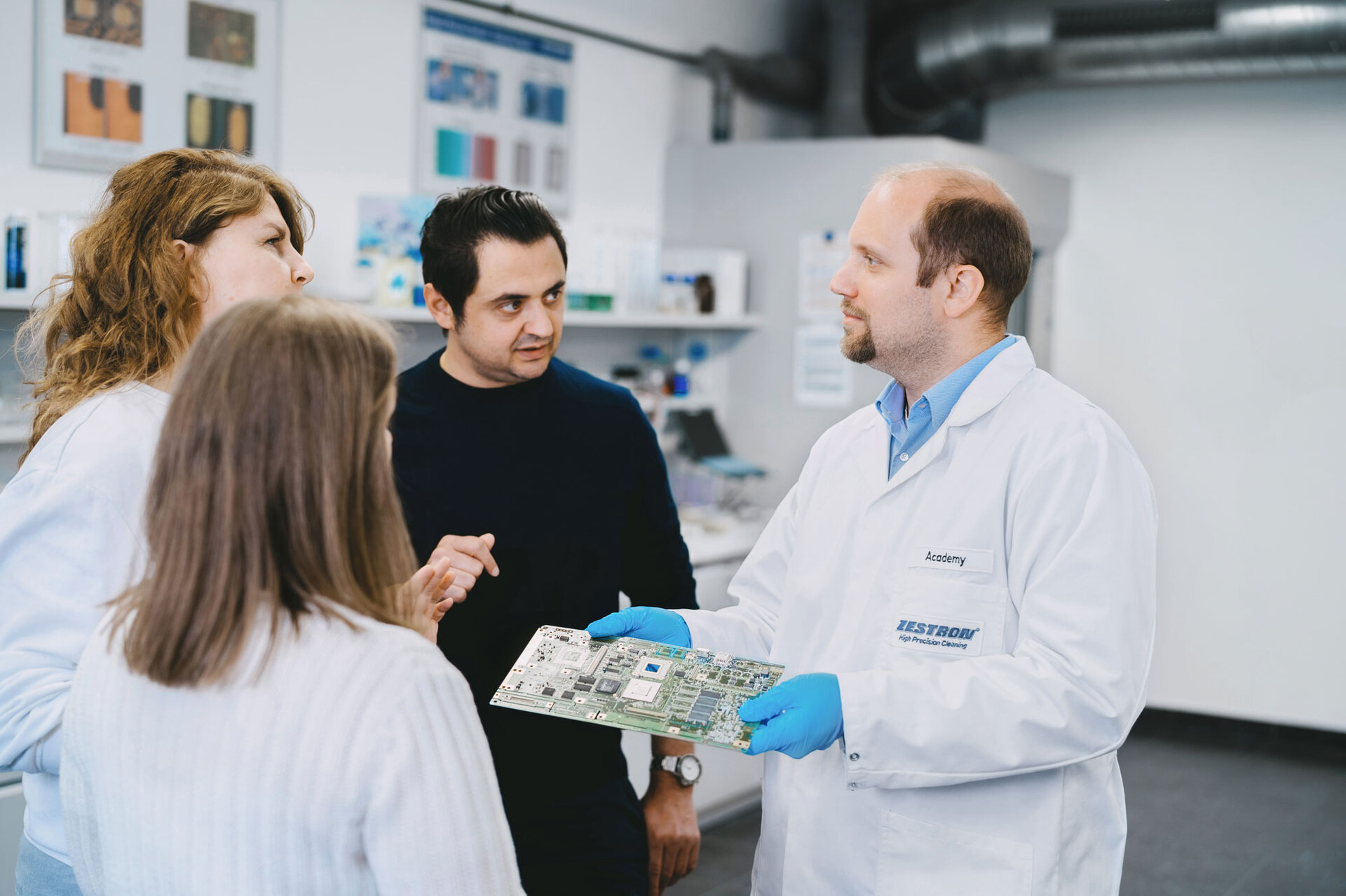 Eine Gruppe von Mitarbeitern diskutiert gemeinsam über die Reinheitsbestimmung elektronischer Baugruppen. | © @The Sour Cherry Fotografie - Michaela Curtis