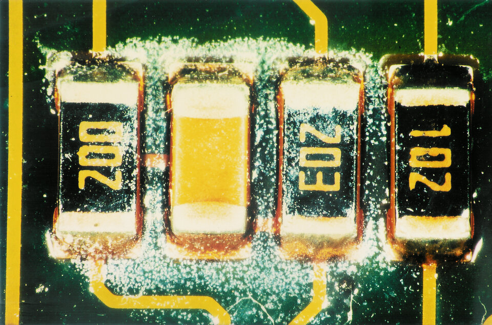 On y voit un gros plan d'un circuit imprimé avec des taches blanches. | © @ZESTRON