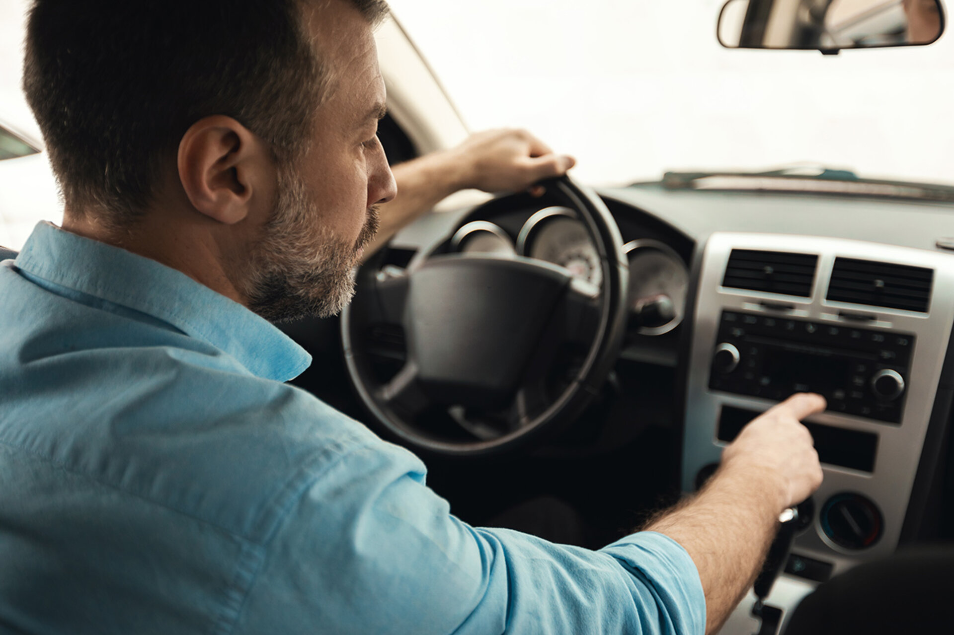 L'image montre un homme dans une voiture en train de faire des réglages de radio.