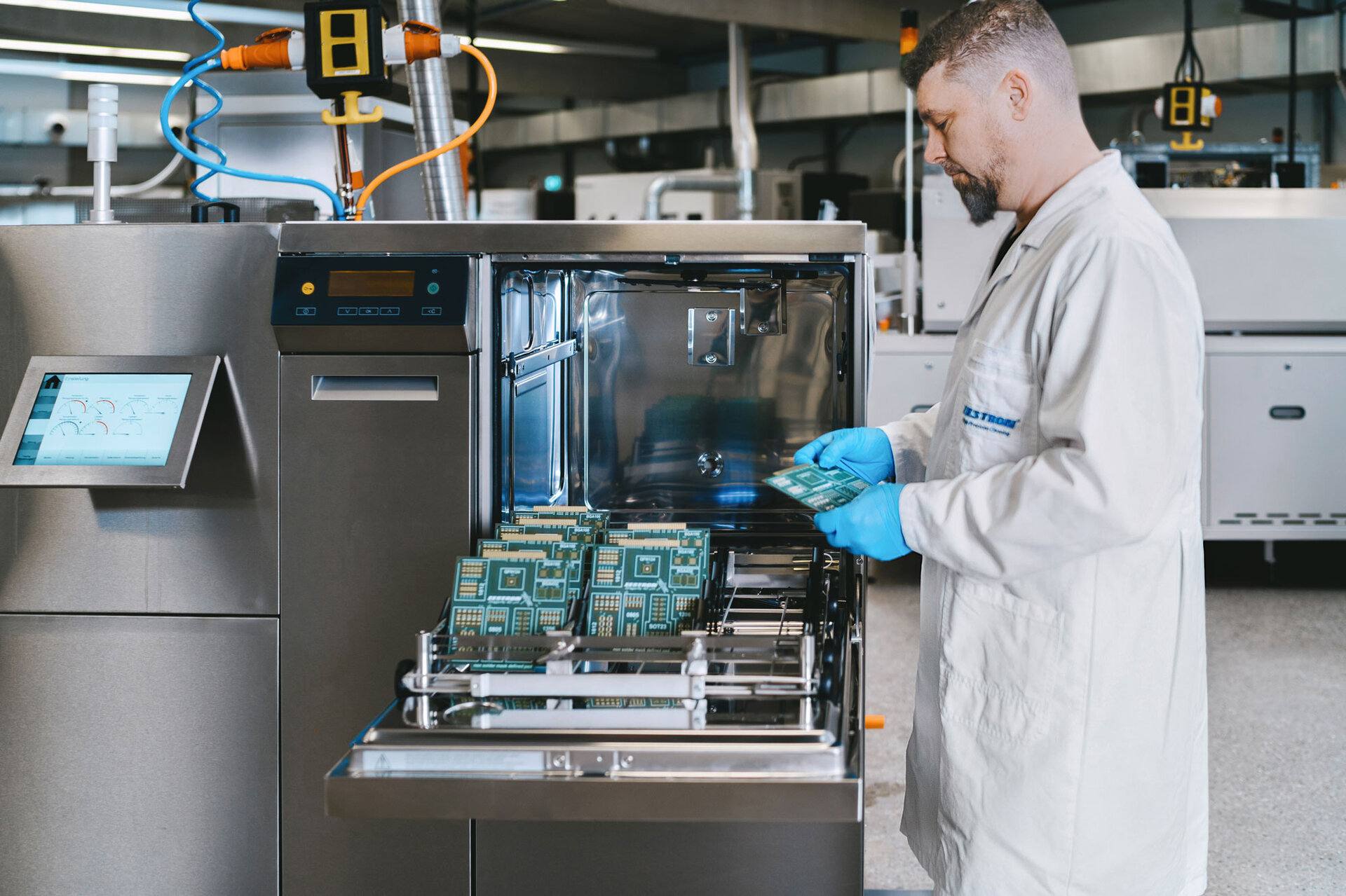 Ein Zestron Ingenieure steht an der Batch-Reinigungsanlage im Maschinen-Testcenter und begutachtet die gereinigten Leiterplatten.  | © @The Sour Cherry Fotografie - Michaela Curtis