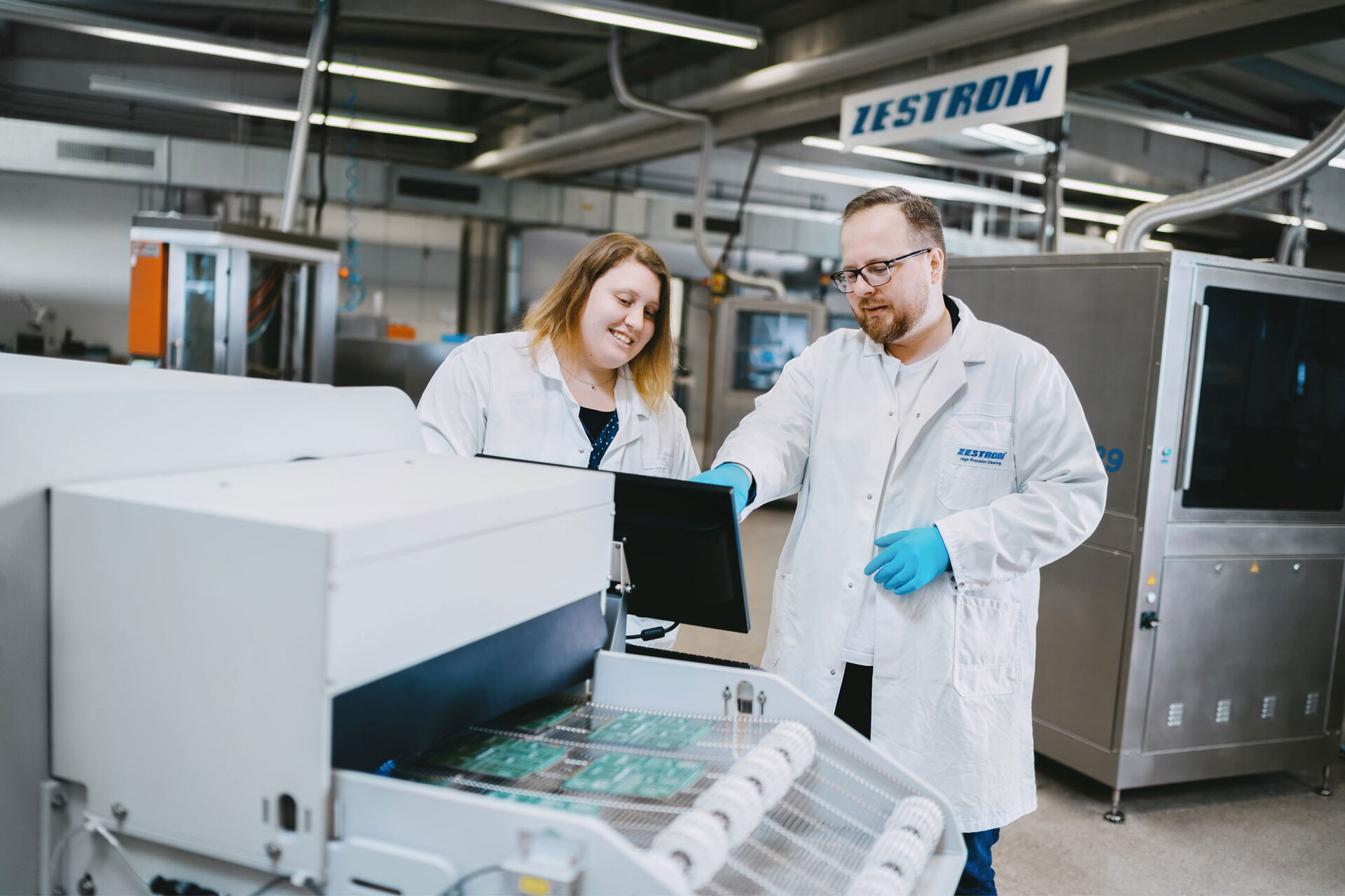 Zwei Techniker stehen vor dem Inline-Reinigungssystem und bewerten die Effizienz der Reinigungsprozesse im Rahmen eines Maschinentests. | © @The Sour Cherry Fotografie - Michaela Curtis