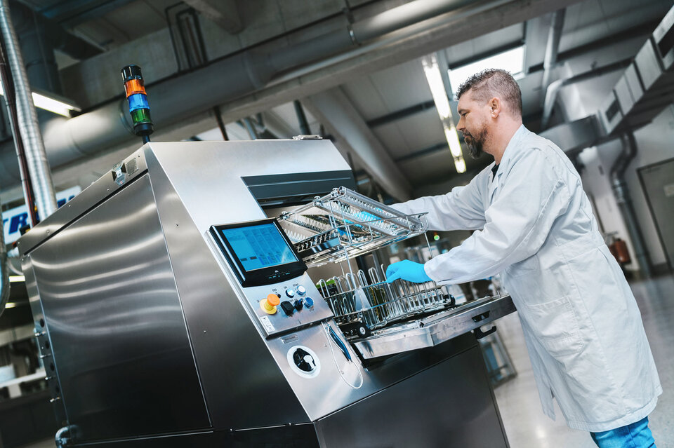 Ein Mitarbeiter steht im technischen Zentrum an der Batch-Reinigungsanlage und bereitet diese für einen Reinigungsvorgang von Leiterplatten vor. | © @The Sour Cherry Fotografie - Michaela Curtis