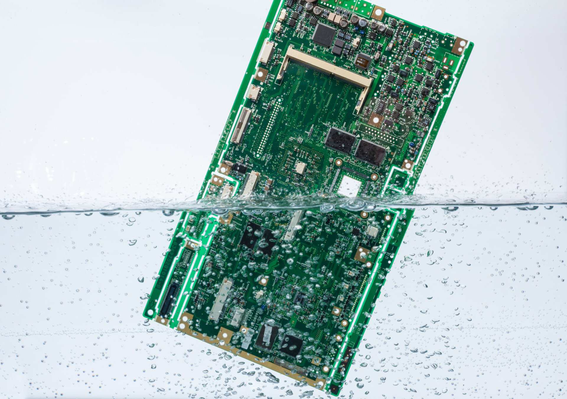 Eine grüne Leiterplatte ist zur Hälfte in Wasser getaucht. | © Zestron