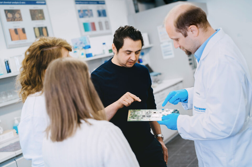 The picture shows a consultation, both the customer and the engineer looking at a circuit board and discussing cleaning processes for electronic assemblies. | © @The Sour Cherry Fotografie - Michaela Curtis